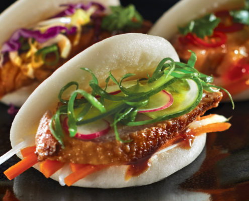 Image of three bao buns; filled with Peking Duck, Korean Chicken, and Roast Pork with accompanying salads