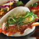 Image of three bao buns; filled with Peking Duck, Korean Chicken, and Roast Pork with accompanying salads