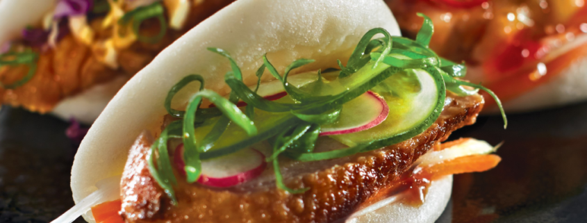 Image of three bao buns; filled with Peking Duck, Korean Chicken, and Roast Pork with accompanying salads