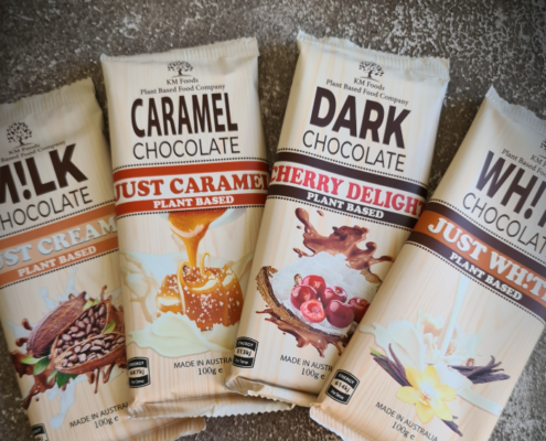 Four packets of Vegan, Plant-based chcolate spread over one another in a small arc. One labelled "Just Creamy", one "Just Caramel", another "Cherry Delight" and the fourth "Just Wh!te"